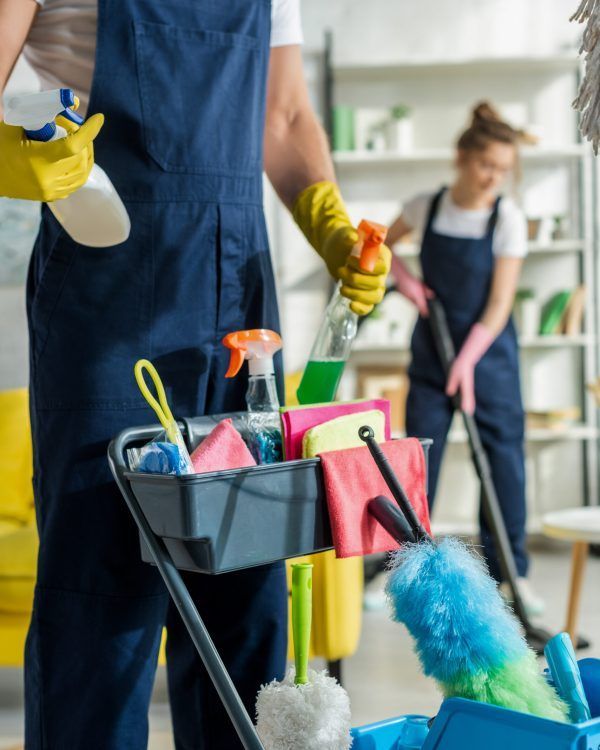 selective focus of cleaner in uniform holding spray bottle near cleaning trolley